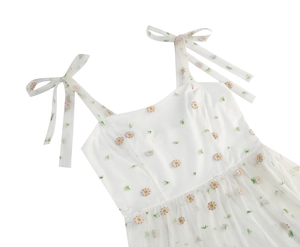 Detailed close-up of white mesh dress featuring delicate daisy embroidery and bow straps