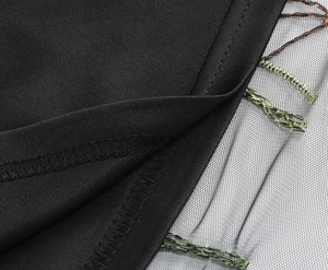 Close-up of intricate embroidery on black mesh fabric with green floral needlework