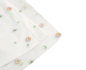 Close-up of delicate daisy embroidery on sheer white mesh fabric for French floral dress