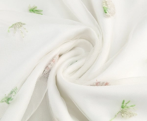 Close-up of delicate floral embroidery on white sheer mesh fabric with soft green stems