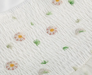 Detail of white smocked fabric with delicate embroidered daisies and green leaves pattern