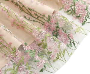 Detailed close-up of floral embroidery on delicate white mesh over pink lining fabric