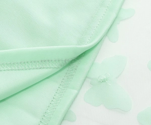 Dettaglio del tessuto verde menta con rivestimento in mesh bianco e farfalle 3D applicate