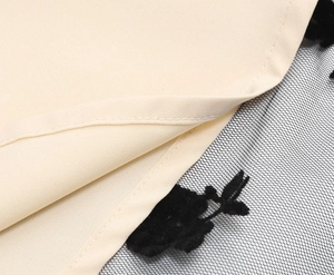 Detailed close-up of beige fabric with black floral mesh overlay and fine stitching