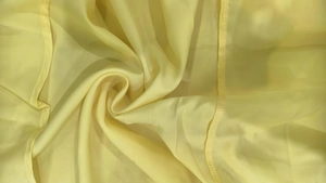 Macro shot of light yellow chiffon fabric showing silky texture and pleated stitching detail