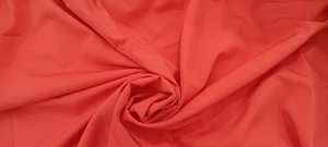 Close-up of vibrant coral red fabric texture with elegant drapes for summer dress.