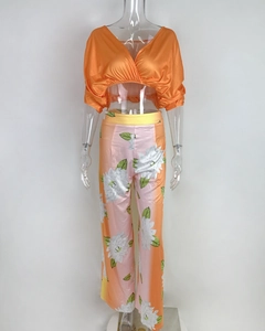 Detailed view of women's two-piece set with orange V-neck wrap top and floral wide-leg pants