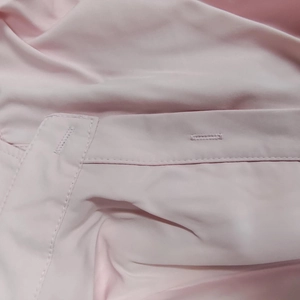 Détail macro des coutures et de la boutonnière du tissu rose de cette robe élégante en V