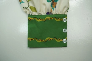 Detail view of green cuffs with wavy patterns and three white buttons on a floral dress