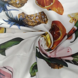 Détail du tissu soyeux avec imprimés de fruits tropicaux comme l'ananas et l'orange