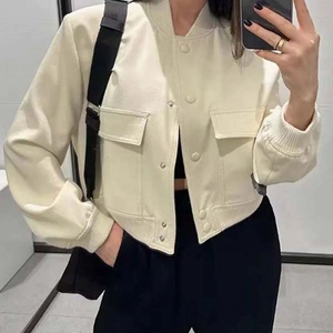 Detalle de chaqueta corta beige con botones metálicos, bolsillos con solapa y puños de canalé