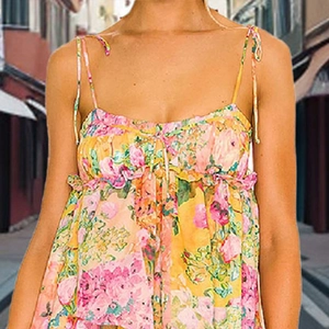 Detail of yellow floral sundress featuring thin straps and ruffled neckline with tie detail
