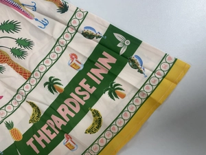 Detail of tropical print fabric with palm trees and Paradise Inn text on a beige dress