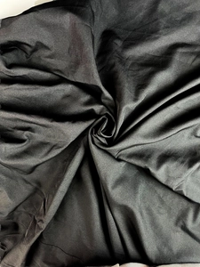 Détail du tissu élégant d'une robe en satin noir montrant la texture lisse et le drapé