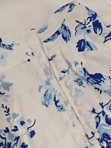 Detail of single-breasted buttons and blue floral print on white chiffon dress
