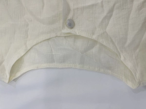 Detailed close-up of cream textured fabric with curved hem and decorative button on dress