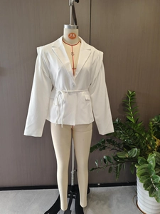 Detail of white blazer featuring lapel collar, waist tie belt, and flap pockets