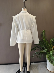 Rear view of white V-neck blazer featuring a waist tie and pleated shoulder details
