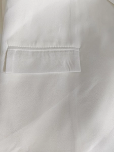 Detailed close-up of pocket flap stitching and fine fabric texture on white blazer