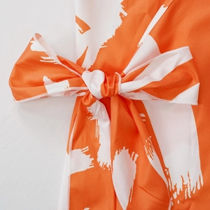 Close-up of artistic orange brushstroke print and fixed bow detail on a floral maxi dress