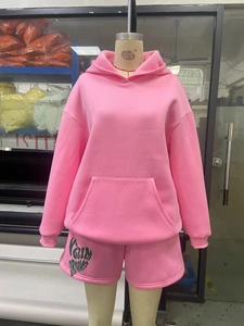 Close-up of pink hoodie and shorts set with green artistic logo print and pouch pocket