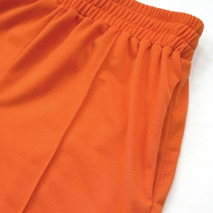 Detail of high waist elastic waistband and side pockets on bright orange casual trousers