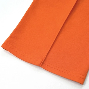 Detailed close-up of double-stitched hem on high-waist bright orange trousers