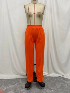 Detail showing bright orange high-waist trousers with elastic waistband and central seam