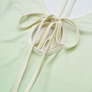 Detail of green V-neck dress featuring lace-up cutout with cream bow and neat stitching
