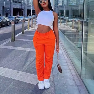 Women's casual outfit featuring white ribbed crop top and orange wide-leg trousers