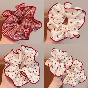 Close-up of four red patterned scrunchies with plaid, cherry, and polka dot designs