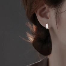 Close-up of textured silver C-shape hoop earrings on model featuring hammered metal finish