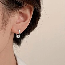 Close-up of a silver hoop earring with sparkling zircon pendant on a model's ear