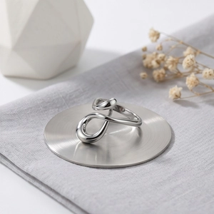 Modern irregular geometric stainless steel ring with a polished mirror finish on a pedestal