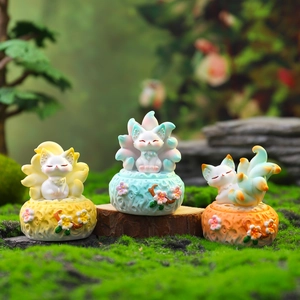 Three Nine-Tailed Fox resin ornaments in yellow and blue, displayed on mossy wood bases
