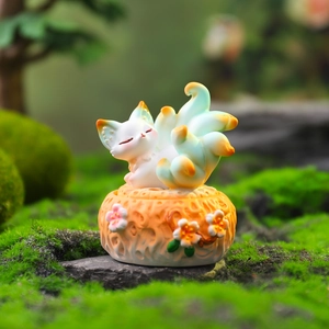 Detail of sleeping nine-tailed fox resin figurine on mossy rock with orange gradient tail
