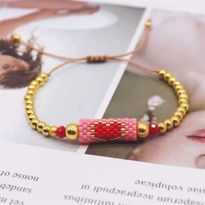 Detail of handmade Miyuki heart bracelet with gold beads and adjustable cord on a magazine