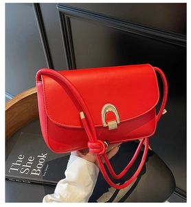 Detail of red square crossbody bag showing large gold horseshoe buckle and knot shoulder strap