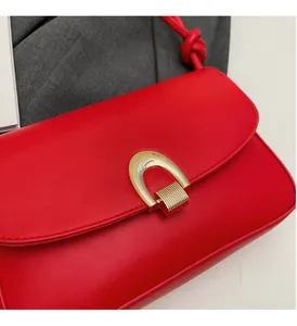 Detail of red leather shoulder bag featuring a golden horseshoe buckle and knotted strap