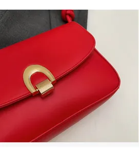 Close-up of vibrant red leather shoulder bag with gold horseshoe metal buckle detail