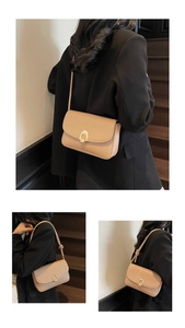 Detail showing the elegant gold curved metal clasp on a beige faux leather shoulder bag