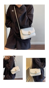 Detail view of white underarm bag featuring a gold horseshoe buckle and knotted strap