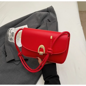 Close-up of a red minimalist baguette bag with a large gold horseshoe buckle and knot detail