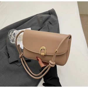 Detail of beige leather bag with a gold horseshoe clasp and twisted shoulder strap