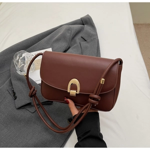 Detail of dark brown leather crossbody bag with gold hardware and knotted strap
