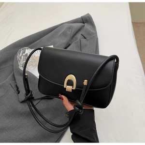 Detail of black leather bag with gold horseshoe buckle on a stylish blazer background