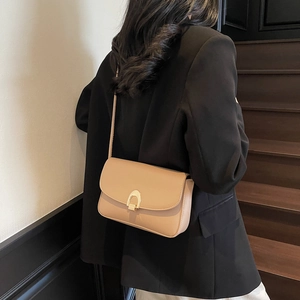 Minimalist beige leather crossbody bag with golden metal buckle worn by a model in a suit
