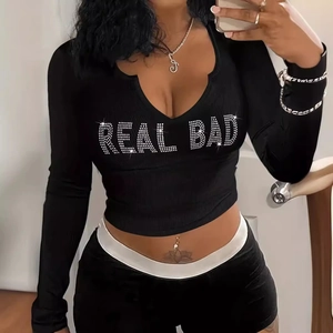Dettaglio del logo REAL BAD in strass scintillanti sul top a maniche lunghe in maglia a coste