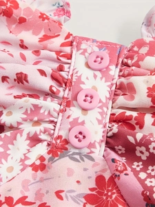 Rosa Kleid mit Blumenmuster, Rüschendetails und Holzknöpfen am vorderen Miederteil