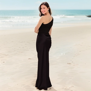 Detailed close-up of a sleek black one-shoulder satin maxi dress on a beach backdrop